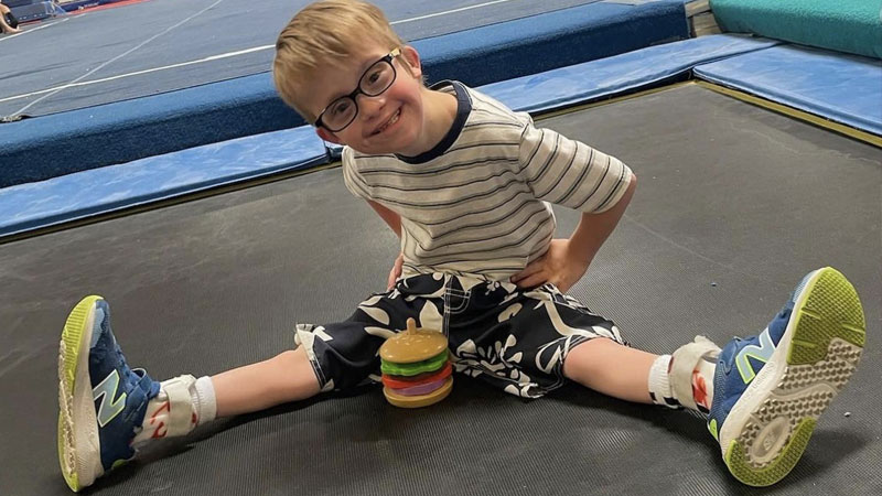 A young boy who uses crutches for walking sits on a gymnastics mat.