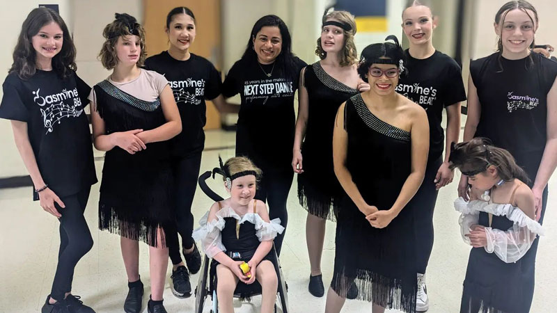 Dancers pose for a photo after a performance. They wear black and white costumes; some have apparent disabilities and one uses a wheelchair.